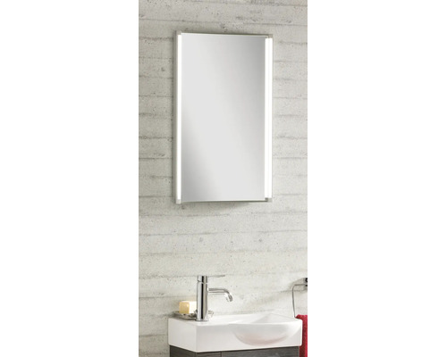 Moderner Badezimmerspiegel mit vertikaler LED-Beleuchtung, weißem Waschbecken und verchromter Armatur vor einer strukturierten Wand.