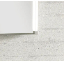 Detailaufnahme der Ecke eines Spiegels mit Metallrahmen und integrierter LED-Seitenbeleuchtung an einer strukturierten Wand.