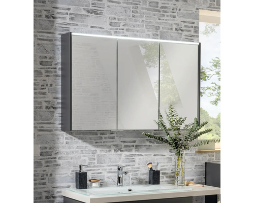 Dreitüriger Spiegelschrank mit LED-Beleuchtung an einer Wand in Steinoptik über einem Waschbecken.