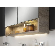 Moderner Badezimmer-Spiegelschrank mit Holzstruktur, beleuchtetem Fach und indirektem Licht unter dem Schrank in einer hellen Badezimmerszene.