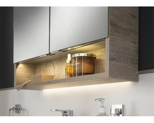 Moderner Badezimmer-Spiegelschrank mit Holzstruktur, beleuchtetem Fach und indirektem Licht unter dem Schrank in einer hellen Badezimmerszene.