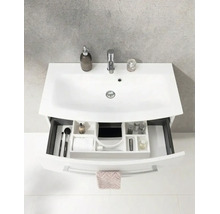 Weißes Waschbecken mit Armatur und Unterschrank mit offener Schublade inklusive Ordnungssystem und Badutensilien.