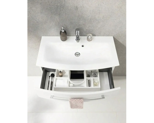 Weißes Waschbecken mit Armatur und Unterschrank mit offener Schublade inklusive Ordnungssystem und Badutensilien.