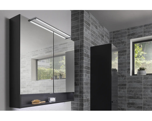 Modernes Badezimmer mit Spiegelschrank aus Glas inklusive LED-Beleuchtung und offener Ablage, Hochschrank und gefliester Wand neben einem Fenster.