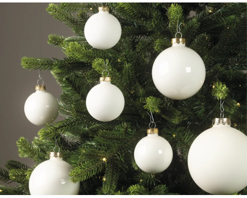 Weiße Christbaumkugeln in matter und glänzender Optik an einem grünen Tannenbaum mit kleinen Lichtern.