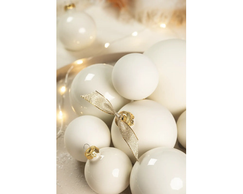 Verschiedene cremeweiße Weihnachtskugeln in matter und glänzender Optik, dekoriert mit einer goldenen Schleife.