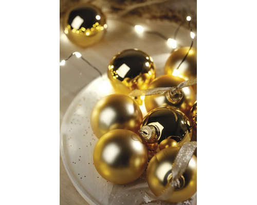 Festliche Anordnung goldener Weihnachtskugeln in glänzender und matter Optik auf einem weißen Teller mit LED-Lichterkette und Dekoband.