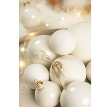 Verschiedene cremeweiße Weihnachtskugeln in matter und glänzender Optik, dekoriert mit einer goldenen Schleife.