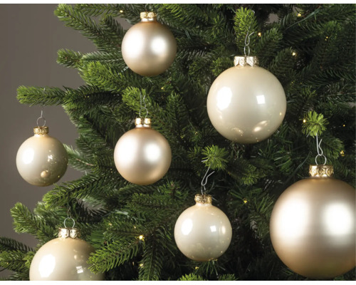 Cremefarbene Weihnachtskugeln in verschiedenen Größen mit glänzender und matter Oberfläche an einem Weihnachtsbaum.