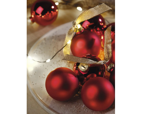 Weihnachtsdekoration mit roten Weihnachtskugeln in matt und glänzend, einem goldenen Dekoband und einer Lichterkette auf einem Teller.