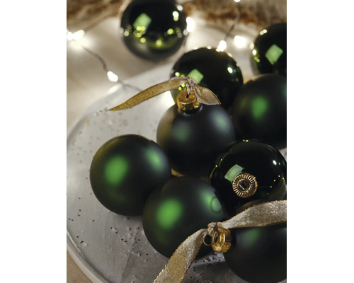 Dunkelgrüne Weihnachtskugeln in matter und glänzender Optik mit goldenen Bändern und festlicher Beleuchtung.