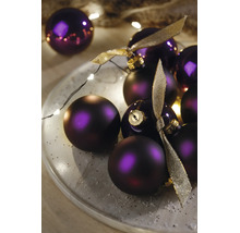 Violette Weihnachtskugeln, matt und glänzend, dekoriert auf einem Teller mit einer LED-Lichterkette und goldenen Schleifen.