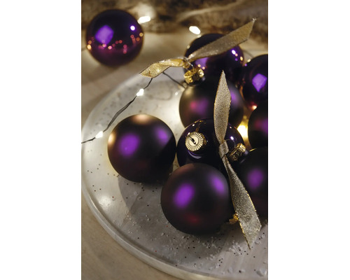 Violette Weihnachtskugeln, matt und glänzend, dekoriert auf einem Teller mit einer LED-Lichterkette und goldenen Schleifen.