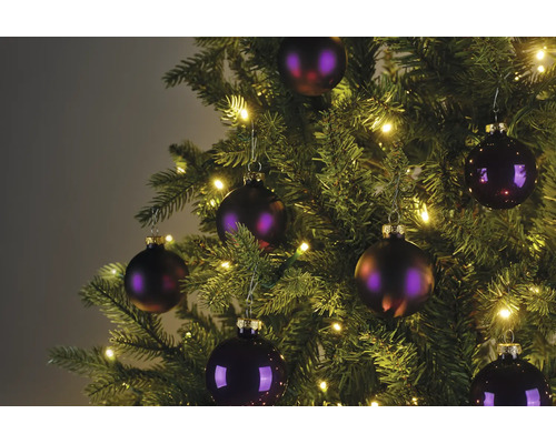 Detailaufnahme eines Weihnachtsbaums mit lila Christbaumkugeln und warmweißer LED-Beleuchtung.