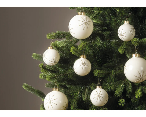 Weiße Weihnachtskugeln mit goldenem Sternmuster an den Zweigen eines grünen Weihnachtsbaums.