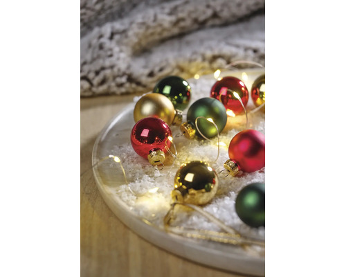 Festliches Arrangement aus Christbaumkugeln in Rot, Grün und Gold auf einem Tablett mit Kunstschnee und LED-Lichterkette.