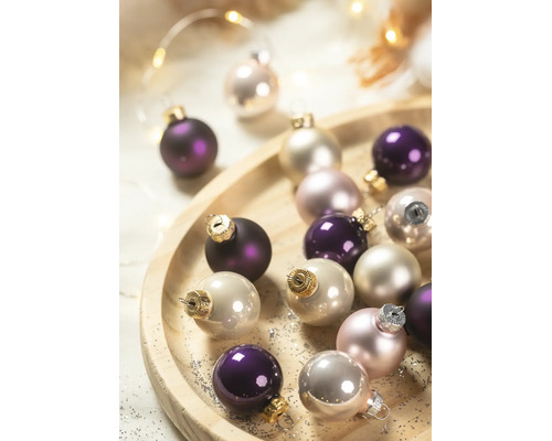Weihnachtskugeln aus Glas in Violett und Creme auf einem runden Holzteller.