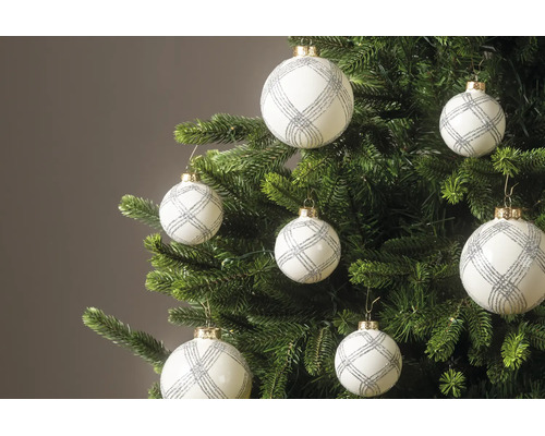 Weiße Weihnachtskugeln mit silbernem Glitzermuster hängen an den Zweigen eines grünen Tannenbaums.