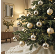 Geschmückter Weihnachtsbaum mit silbernen und champagnerfarbenen Kugeln, Lichterkette und goldenen Girlanden in einem hellen Wohnzimmer.