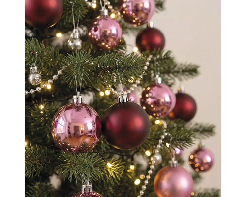 Weihnachtsbaum dekoriert mit glänzenden rosa und matten dunkelroten Weihnachtskugeln, einer Perlenkette und einer warmweißen Lichterkette.
