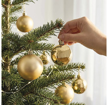 Eine Hand hängt eine glänzende goldene Weihnachtskugel an einen Tannenbaum mit weiteren matten und glänzenden Kugeln.