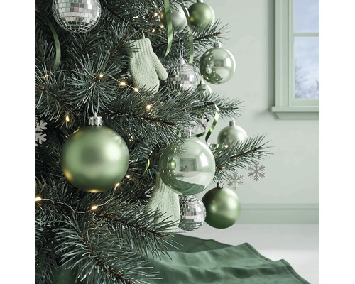 Weihnachtsbaum dekoriert mit grünen Kugeln, silbernen Discokugeln, kleinen Fäustlingen und einer Lichterkette in einem hellen Raum.