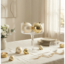 Weihnachtskugeln mit glänzender und matter Oberfläche, arrangiert in einer Glasschale auf einem gedeckten Tisch mit Kerzen und Geschirr.