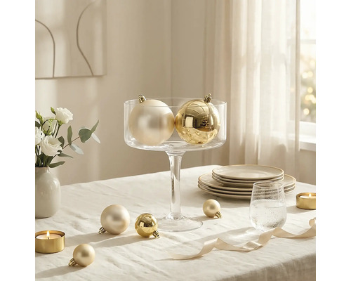 Weihnachtskugeln mit glänzender und matter Oberfläche, arrangiert in einer Glasschale auf einem gedeckten Tisch mit Kerzen und Geschirr.