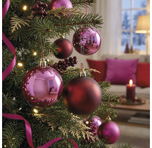 Geschmückter Christbaum mit glänzenden und matten Christbaumkugeln, Beeren und Bändern in einem gemütlichen, hellen Wohnzimmer.