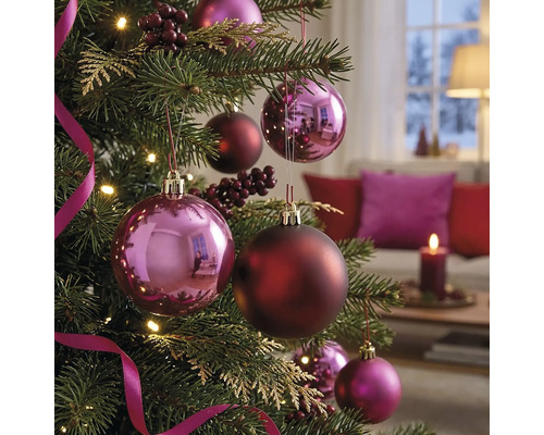 Geschmückter Christbaum mit glänzenden und matten Christbaumkugeln, Beeren und Bändern in einem gemütlichen, hellen Wohnzimmer.