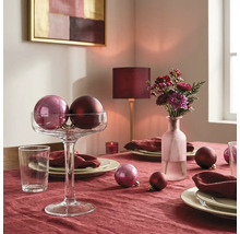 Festlich gedeckter Tisch mit Tischdecke, Christbaumkugeln in einer Glasschale auf Fuß, Blumenvase, Tellern und Servietten.