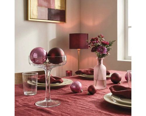 Festlich gedeckter Tisch mit Tischdecke, Christbaumkugeln in einer Glasschale auf Fuß, Blumenvase, Tellern und Servietten.