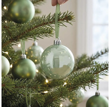 Transparente Weihnachtskugel aus Glas an einem beleuchteten Weihnachtsbaum, aufgehängt mit einem Band.