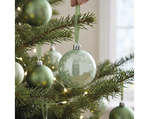 Transparente Weihnachtskugel aus Glas an einem beleuchteten Weihnachtsbaum, aufgehängt mit einem Band.