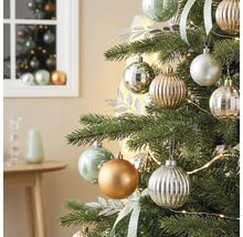 Christbaum geschmückt mit matten, glänzenden und geriffelten Kugeln, silbernen Dekoblättern und einer Lichterkette in einem hellen Zimmer.