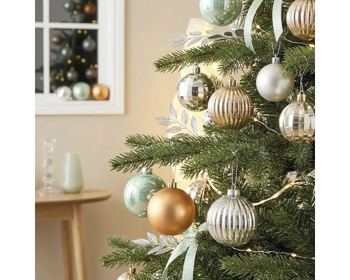Christbaum geschmückt mit matten, glänzenden und geriffelten Kugeln, silbernen Dekoblättern und einer Lichterkette in einem hellen Zimmer.