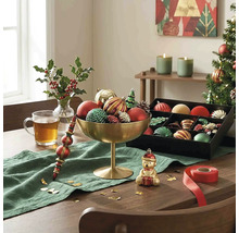 Festlich dekorierter Holztisch mit goldener Schale voller Weihnachtsschmuck, einer schwarzen Sortierbox, grünem Läufer und Teeglas.