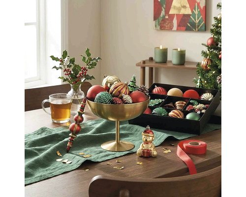 Festlich dekorierter Holztisch mit goldener Schale voller Weihnachtsschmuck, einer schwarzen Sortierbox, grünem Läufer und Teeglas.