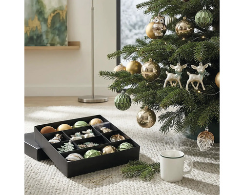 Weihnachtsbaum geschmückt mit Christbaumkugeln, Eulen- und Hirschfiguren neben einer Aufbewahrungsbox mit Weihnachtsschmuck auf einem Teppich.