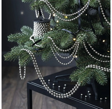 Silberne Perlenkette an den Zweigen eines Christbaums mit warmweißen Lichtern.