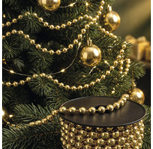 Weihnachtsbaum geschmückt mit goldener Perlenkette und Weihnachtskugeln, im Vordergrund eine Spule mit der goldenen Perlenkette.