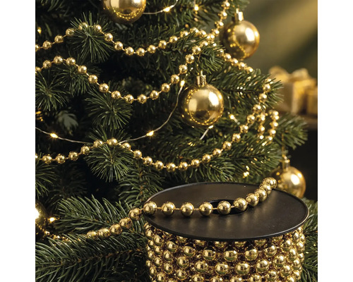 Weihnachtsbaum geschmückt mit goldener Perlenkette und Weihnachtskugeln, im Vordergrund eine Spule mit der goldenen Perlenkette.