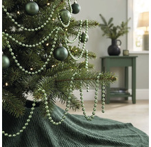 Dekorierter Weihnachtsbaum mit matten Kugeln, einer Perlenkette und einer gestrickten Weihnachtsbaumdecke in einem Wohnzimmer.