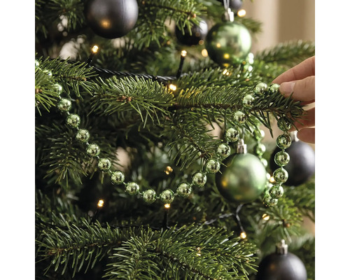 Perlenkette für den Weihnachtsbaum, dekoriert an einem Tannenbaum mit Christbaumkugeln und Lichterkette.
