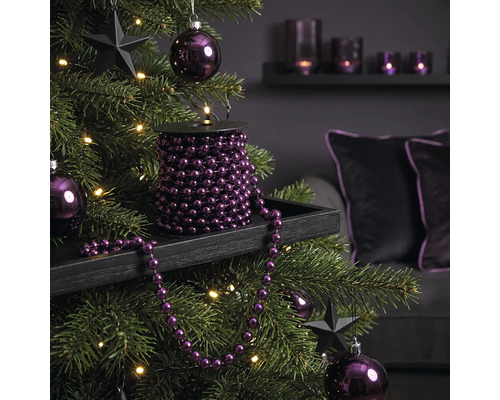 Weihnachtsbaum dekoriert mit lila Perlengirlande auf einer Spule, lila Christbaumkugeln, schwarzen Sternen und Lichterkette.