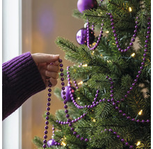 Eine Hand dekoriert einen Christbaum mit einer lila Perlengirlande, Christbaumkugeln und warmweißer Beleuchtung.
