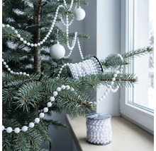 Weiße Perlenkette als Weihnachtsbaumschmuck auf einem Christbaum dekoriert, Christbaumkugeln und eine Rolle Perlen auf der Fensterbank.