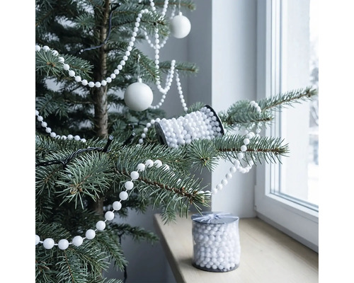 Weiße Perlenkette als Weihnachtsbaumschmuck auf einem Christbaum dekoriert, Christbaumkugeln und eine Rolle Perlen auf der Fensterbank.