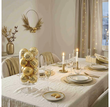 Festlich gedeckter Esstisch mit goldenen Weihnachtskugeln in einem Glaszylinder, Kerzen, goldenem Besteck und elegantem Geschirr.