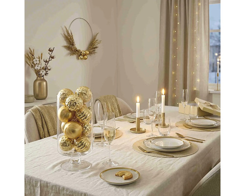 Festlich gedeckter Esstisch mit goldenen Weihnachtskugeln in einem Glaszylinder, Kerzen, goldenem Besteck und elegantem Geschirr.